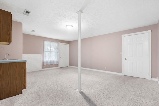 unfurnished living room featuring a sink, light colored carpet, baseboards, and a textured ceiling