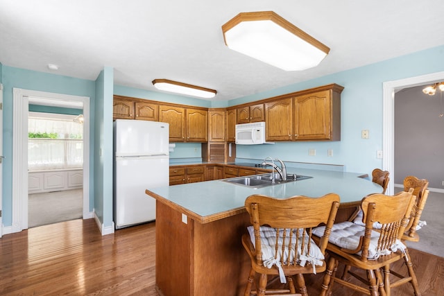 kitchen with white appliances, a sink, brown cabinets, a peninsula, and wood finished floors