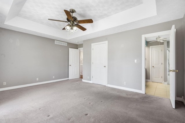 unfurnished bedroom featuring a raised ceiling, carpet flooring, baseboards, and ceiling fan