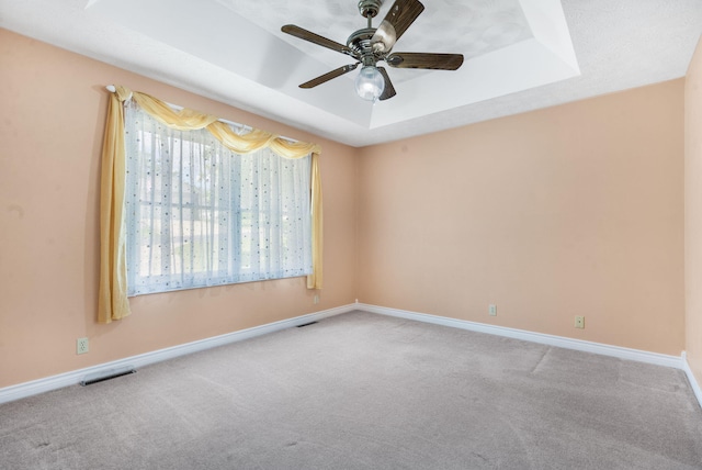 carpeted spare room with a raised ceiling, a ceiling fan, and baseboards