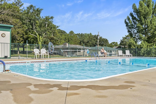 community pool with fence, a patio, and view of wooded area