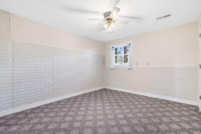 spare room featuring carpet floors, ceiling fan, brick wall, and baseboards