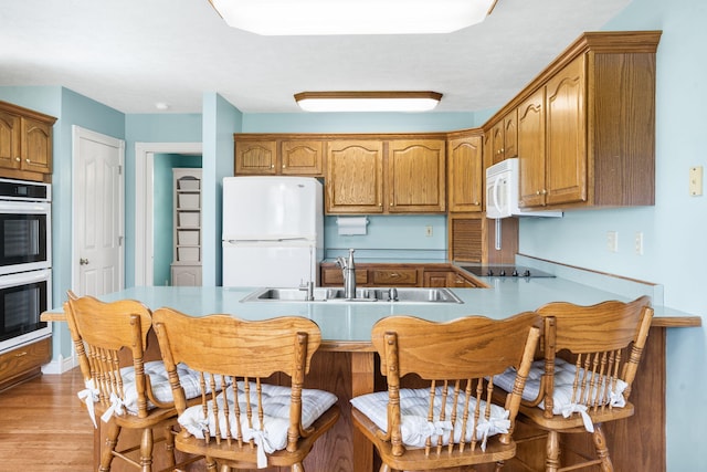 kitchen with white appliances, a sink, and brown cabinetry