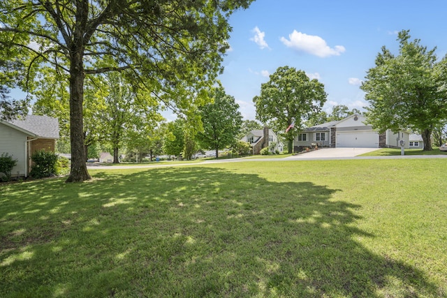 view of green lawn with driveway, an attached garage, and a residential view