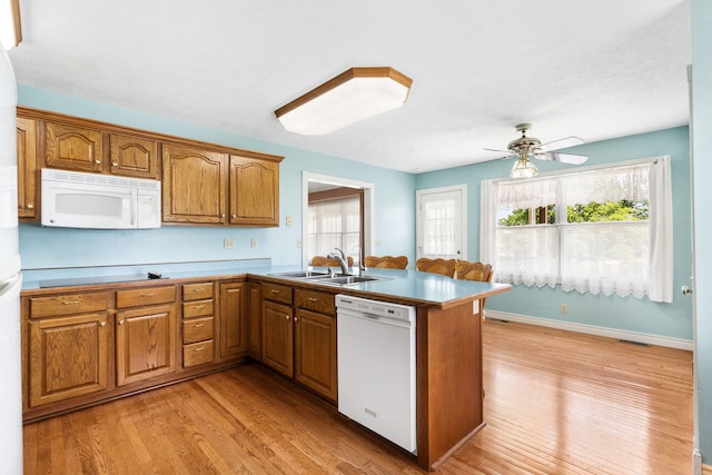 kitchen with white appliances, a sink, brown cabinets, a peninsula, and light wood-style flooring