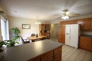 kitchen with white fridge with ice dispenser, brown cabinets, a ceiling fan, a chandelier, and light floors