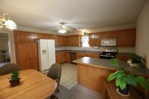 kitchen with appliances with stainless steel finishes, brown cabinets, ceiling fan, a peninsula, and light flooring