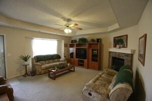 living area featuring ceiling fan, a fireplace, a raised ceiling, and carpet flooring