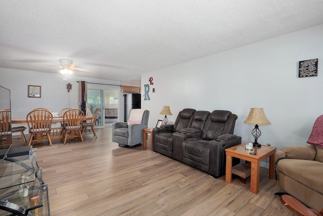 living area featuring light wood-type flooring, a textured ceiling, and ceiling fan