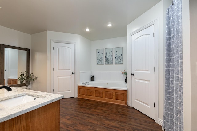 full bathroom with wood finished floors, a garden tub, vanity, and recessed lighting