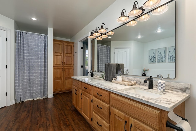 bathroom with wood finished floors, double vanity, recessed lighting, and baseboards