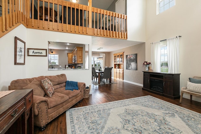living area featuring dark wood-type flooring, baseboards, a high ceiling, and a chandelier