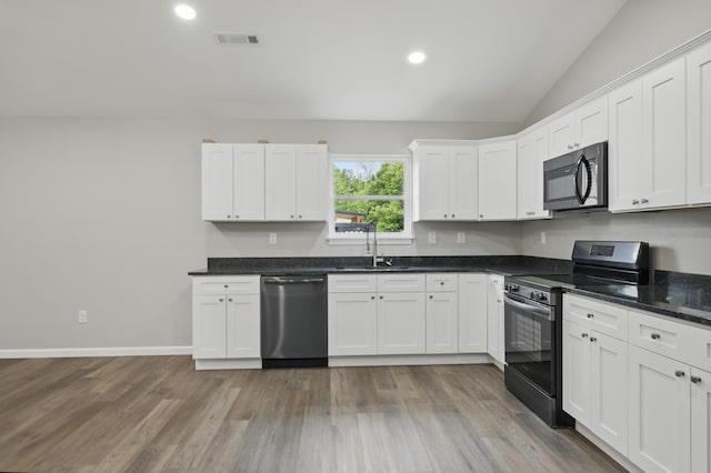 kitchen with stainless steel appliances, a sink, white cabinets, vaulted ceiling, and light wood finished floors