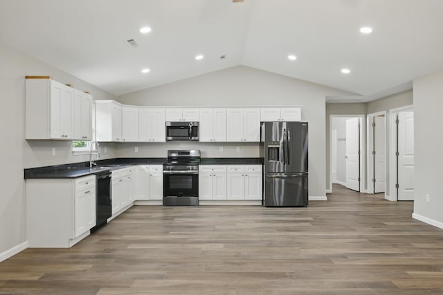 kitchen with stainless steel appliances, vaulted ceiling, dark countertops, white cabinetry, and baseboards