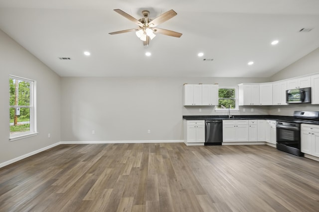 kitchen featuring stainless steel appliances, lofted ceiling, dark countertops, light wood finished floors, and white cabinets