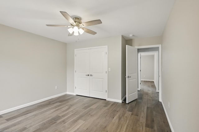 unfurnished bedroom featuring wood finished floors, a closet, baseboards, and a ceiling fan