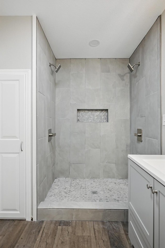 bathroom featuring wood finished floors, a tile shower, and vanity