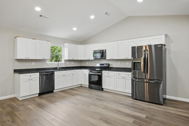kitchen featuring appliances with stainless steel finishes, vaulted ceiling, white cabinetry, dark countertops, and light wood-type flooring