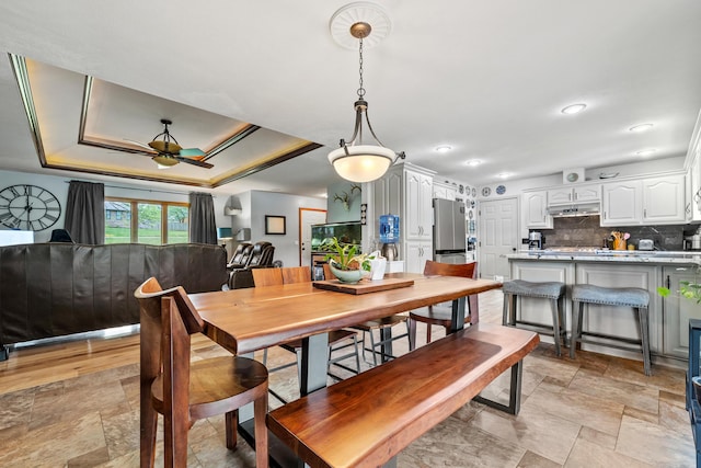 dining area with ceiling fan, light stone finish flooring, a tray ceiling, and recessed lighting