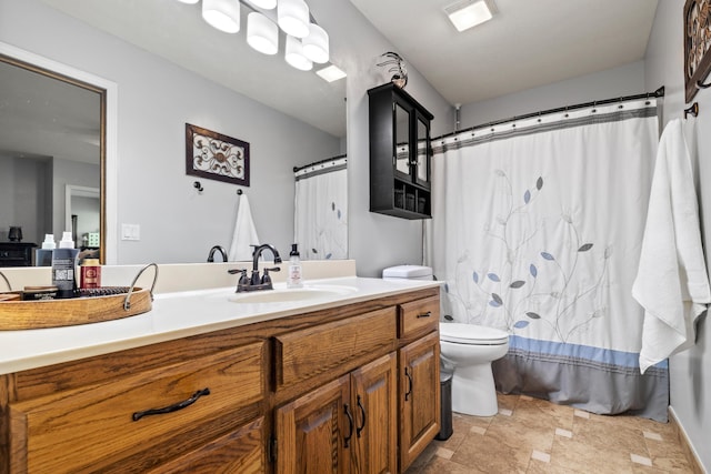 bathroom featuring toilet, vanity, stone finish flooring, and curtained shower