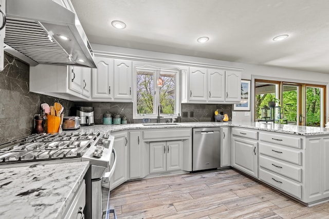 kitchen with appliances with stainless steel finishes, extractor fan, a sink, a peninsula, and white cabinetry