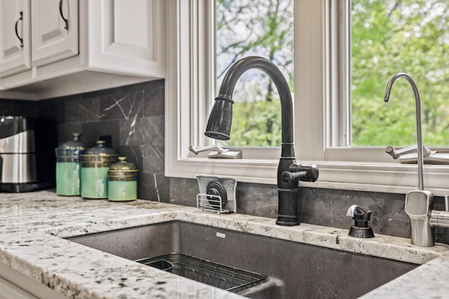 kitchen view of a sink, tasteful backsplash, and light stone counters