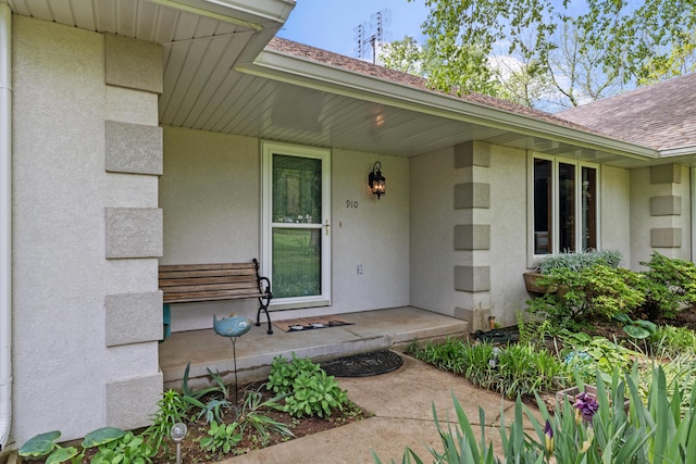 entrance to property with a porch, roof with shingles, and stucco siding