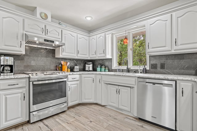 kitchen with appliances with stainless steel finishes, under cabinet range hood, a sink, and white cabinetry