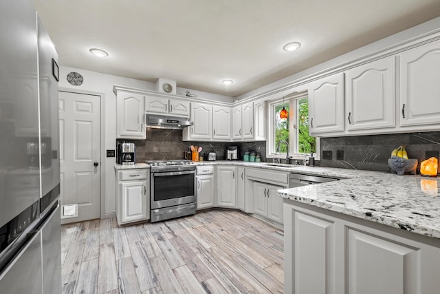 kitchen with stainless steel appliances, under cabinet range hood, a sink, and white cabinetry