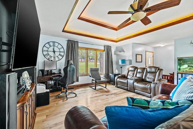 living area featuring a tray ceiling, a ceiling fan, light wood finished floors, and a desk