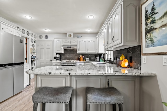 kitchen with freestanding refrigerator, a peninsula, a sink, a kitchen breakfast bar, and light stone countertops