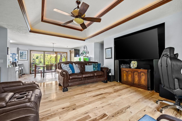 living room featuring a tray ceiling, light wood finished floors, a ceiling fan, and crown molding