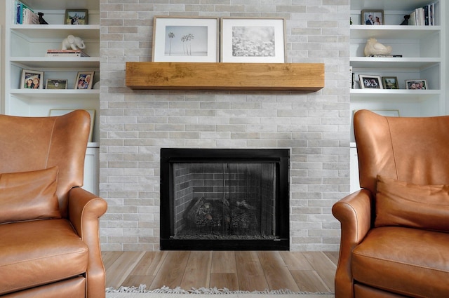 sitting room with wood finished floors, a fireplace, and built in shelves