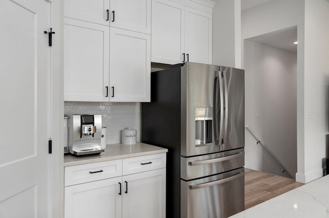 kitchen with stainless steel fridge, decorative backsplash, white cabinetry, light wood-style floors, and light stone countertops