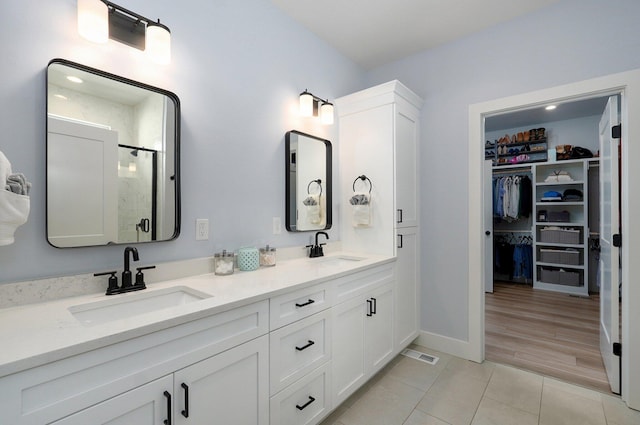 full bathroom with tile patterned floors, a stall shower, a spacious closet, double vanity, and baseboards