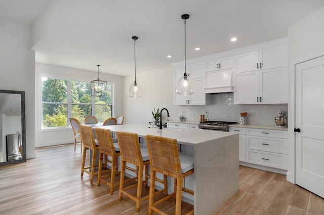 kitchen with custom exhaust hood, stainless steel gas range, light wood-style flooring, tasteful backsplash, and white cabinetry