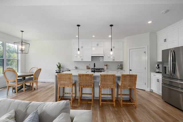 kitchen with stainless steel refrigerator with ice dispenser, a chandelier, light wood-type flooring, backsplash, and open floor plan