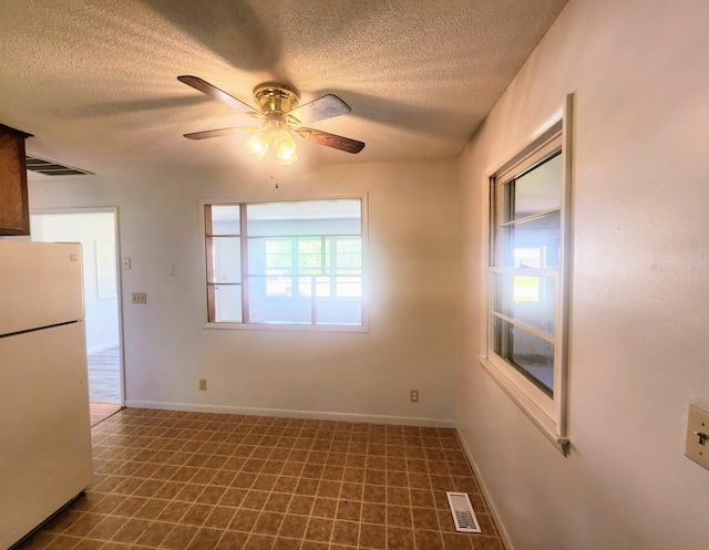 empty room featuring a textured ceiling, a ceiling fan, dark flooring, and baseboards