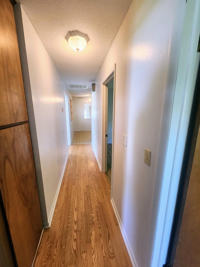 hall with light wood-style flooring, a textured ceiling, and baseboards