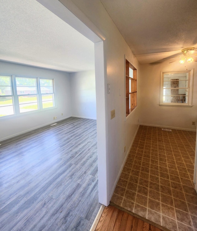 empty room featuring a textured ceiling, wood finished floors, baseboards, and a ceiling fan