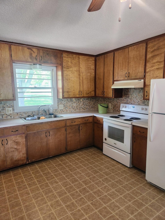 kitchen with white appliances, under cabinet range hood, a sink, tile patterned floors, and a textured ceiling