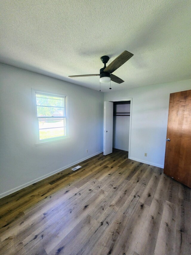 unfurnished bedroom featuring wood finished floors, a textured ceiling, baseboards, ceiling fan, and a closet