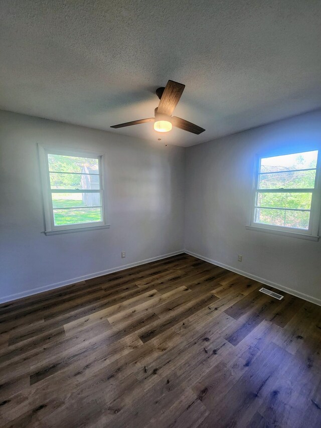 unfurnished room featuring plenty of natural light, dark wood-type flooring, a textured ceiling, baseboards, and ceiling fan