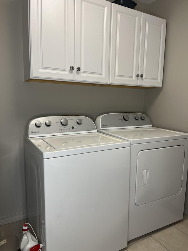 clothes washing area featuring washer and clothes dryer, cabinet space, and light tile patterned flooring