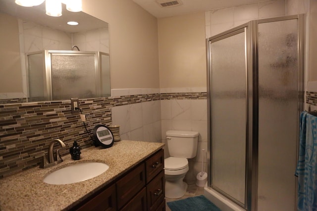 bathroom featuring a stall shower, vanity, toilet, tile walls, and tile patterned flooring