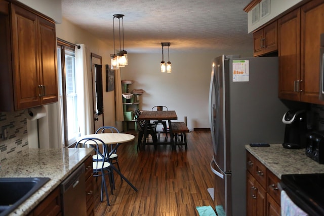kitchen with appliances with stainless steel finishes, dark wood-style floors, tasteful backsplash, pendant lighting, and brown cabinetry