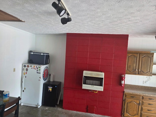 kitchen featuring heating unit, freestanding refrigerator, unfinished concrete flooring, a textured ceiling, and brown cabinetry