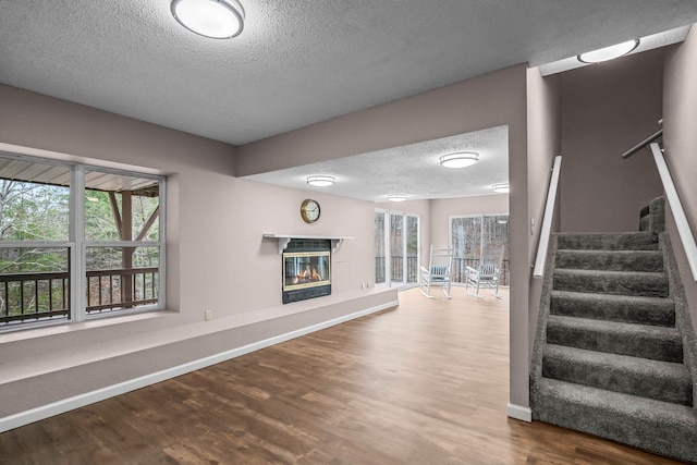 70 Roseville Dr, Rogersville, MO 65742 - unfurnished living room with a textured ceiling, wood finished floors, a glass covered fireplace, stairway, and healthy amount of natural light
