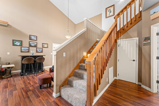 stairs featuring a towering ceiling, wood finished floors, and baseboards