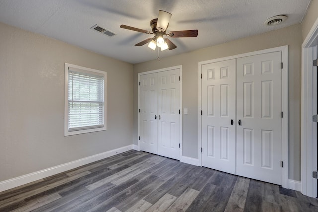 unfurnished bedroom featuring dark wood-style flooring, baseboards, a textured ceiling, ceiling fan, and multiple closets